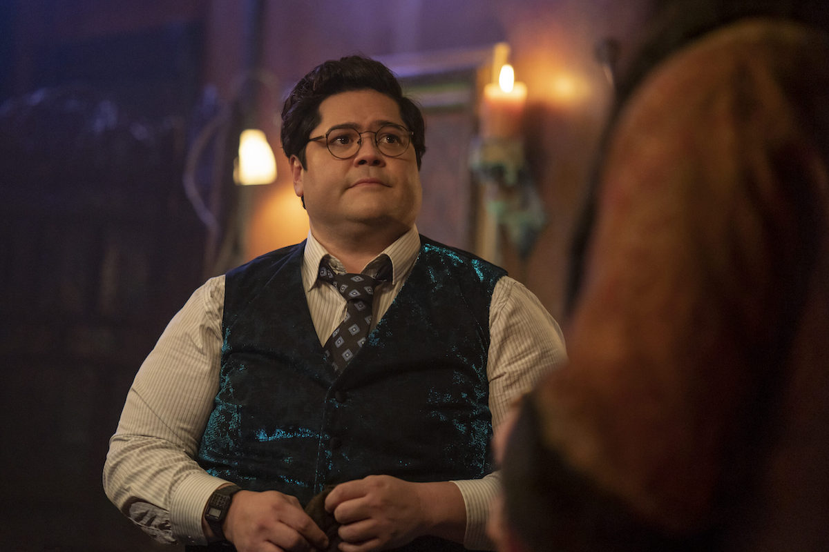 Guillermo looks pensively at Nandor, whose shoulder is visible in the foreground of the shot.