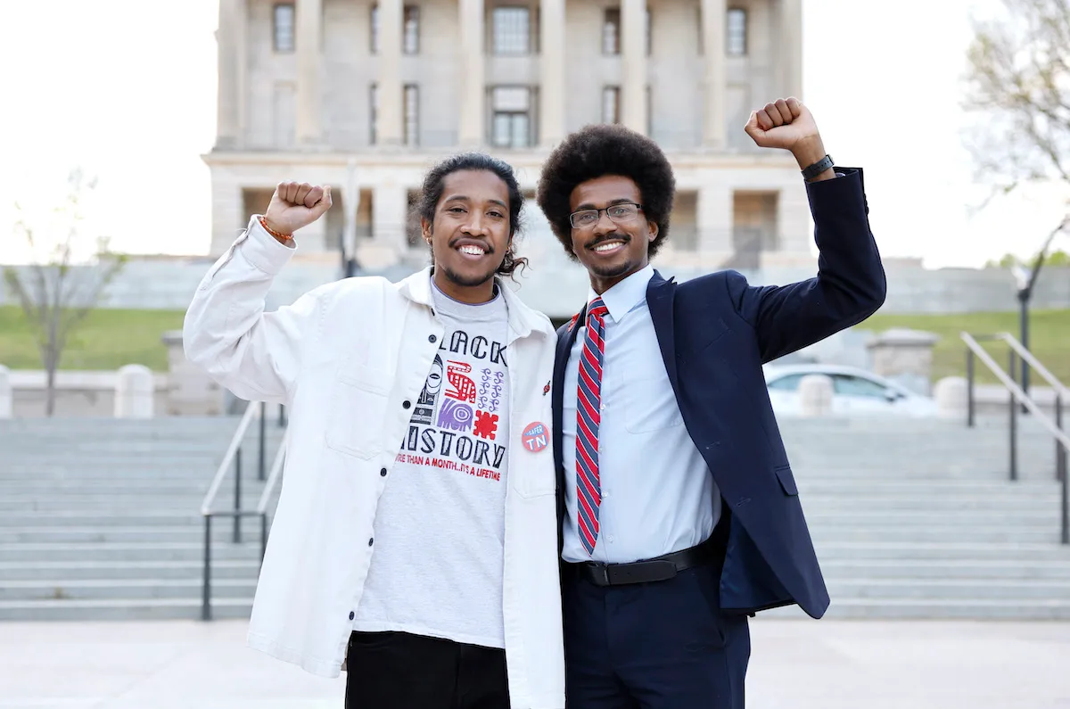 Tennessee State Representatives Justin Jones and Justin J. Pearson stand together smiling and raising their fists in the air.