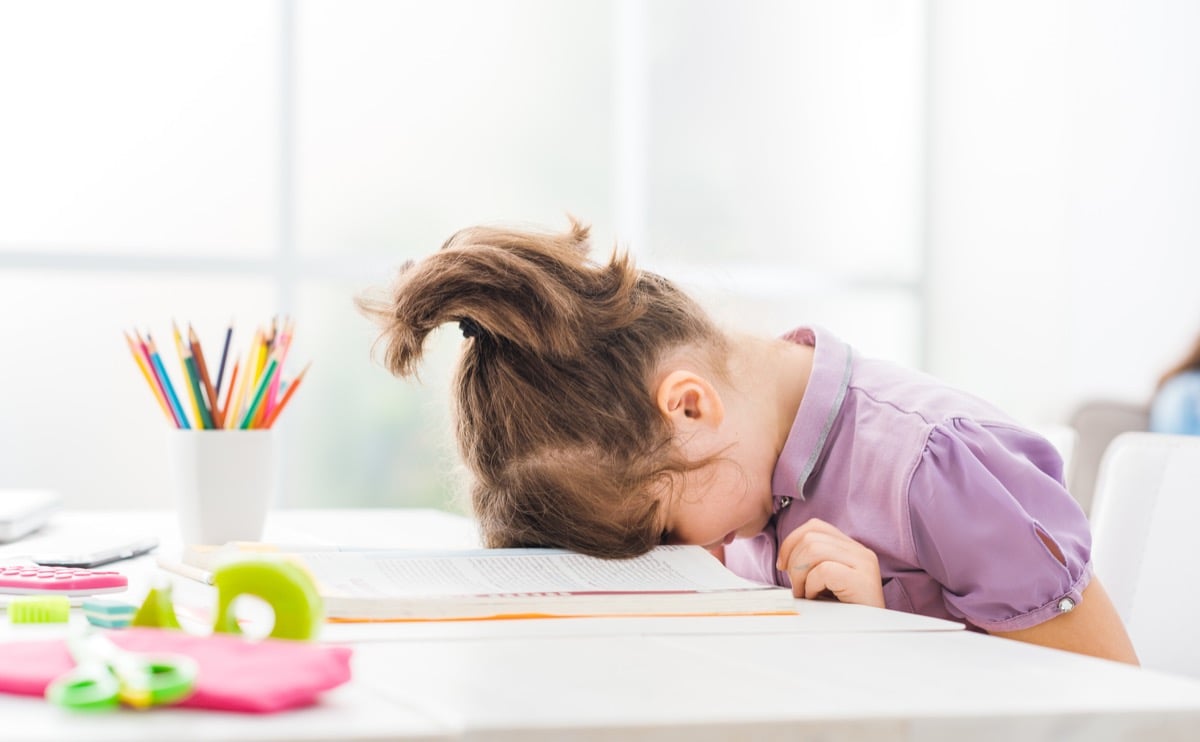 A young child with her face resting on a book in frustration.