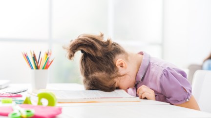 A young child with her face resting on a book in frustration.