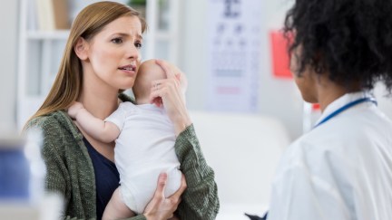 Worried new mom comforts her newborn baby while talking with the child's pediatrician.