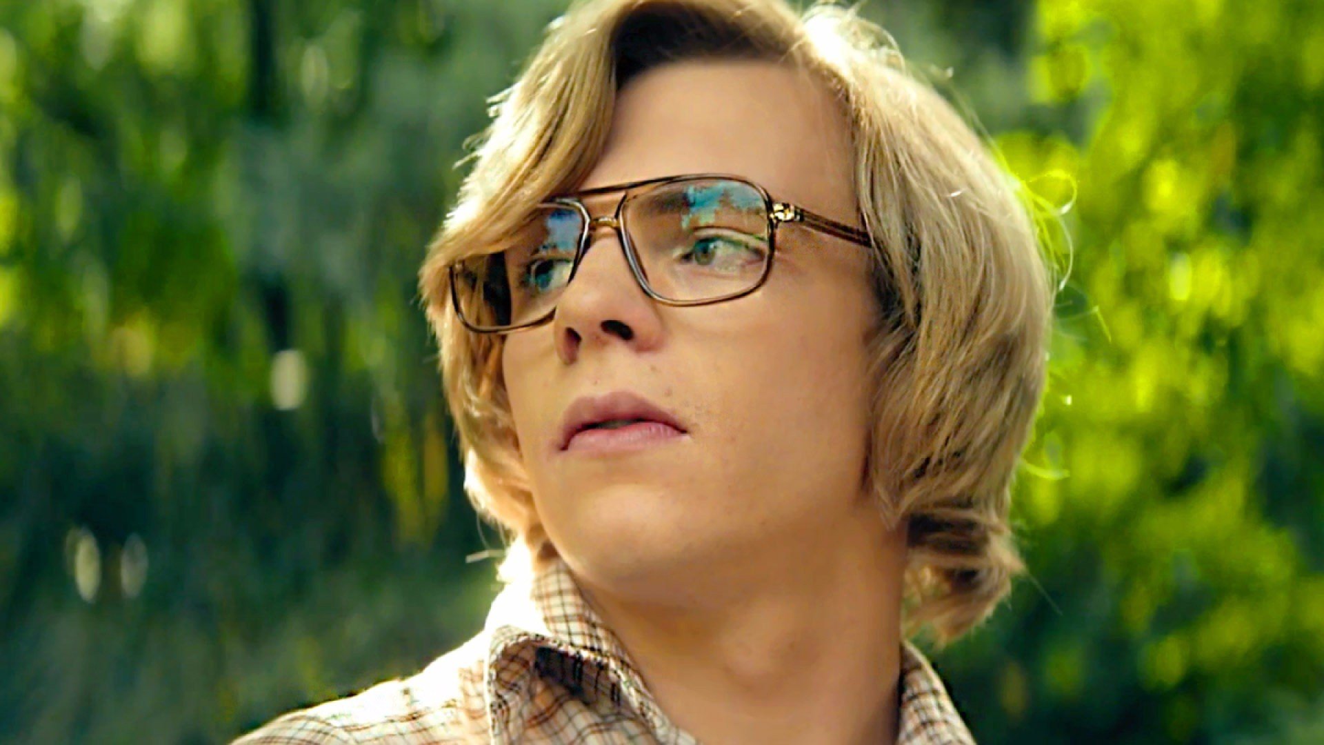 A young blond white man with aviator style reading glasses stare away towards the sun