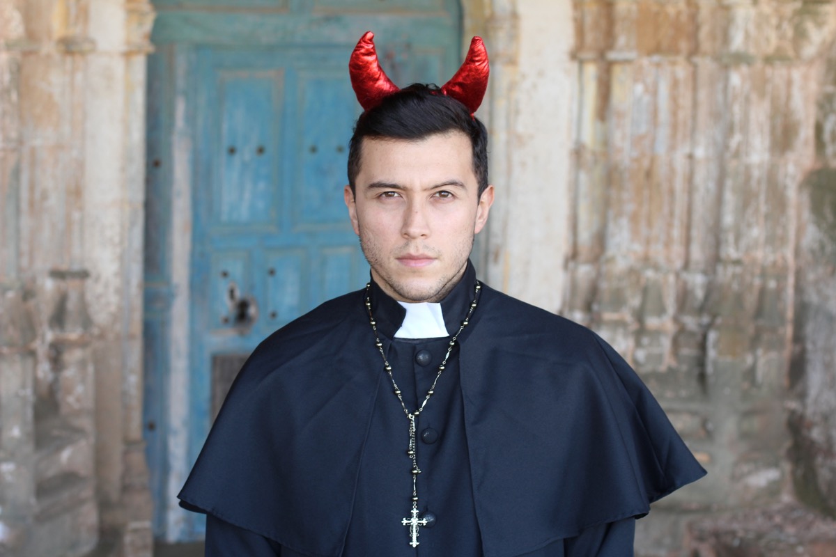 A priest wearing red, sparkly costume devil horns on his head.