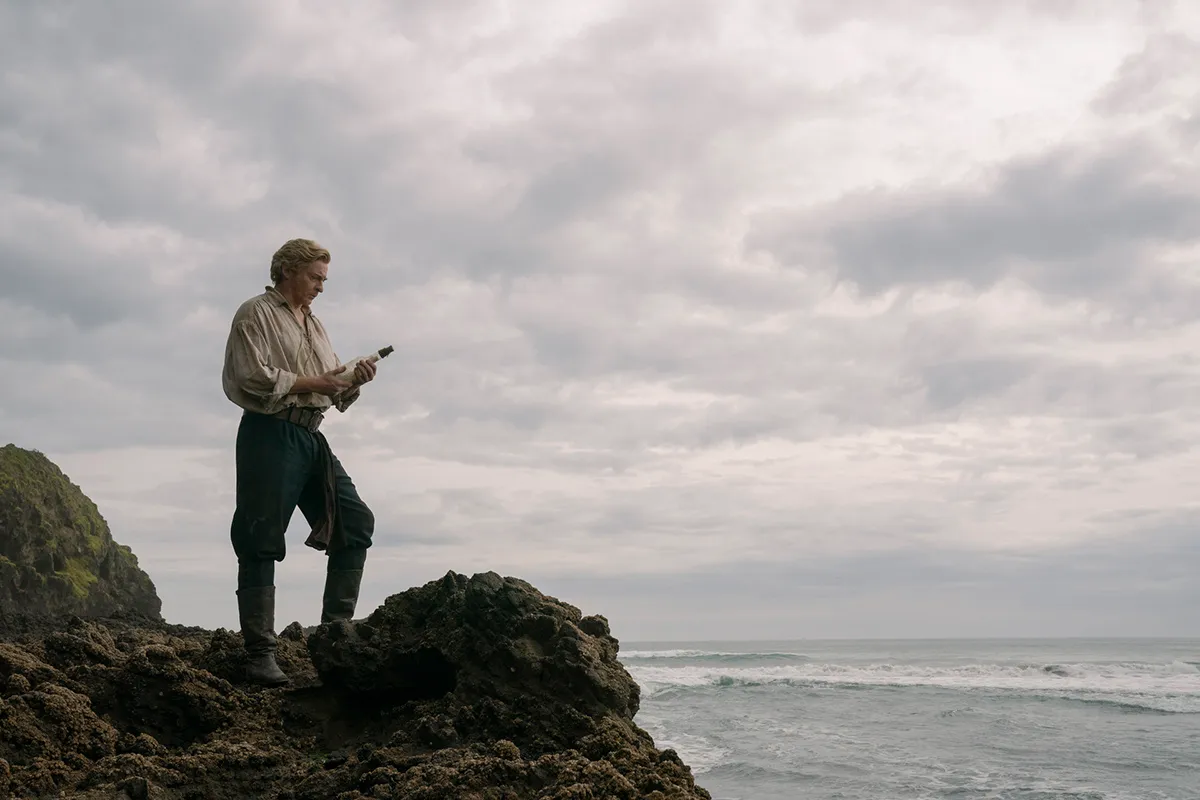 Stede Bonnet (Rhys Darby) holds a message in a bottle while looking out on a cliff in 'Our Flag Means Death'.
