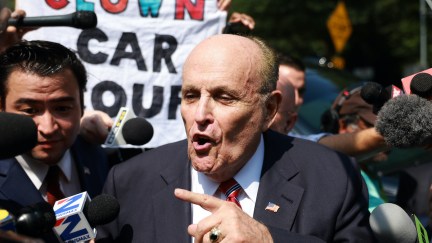 Rudy Giuliani speaks to the media after leaving the Fulton County jail. A sign held behind him reads 