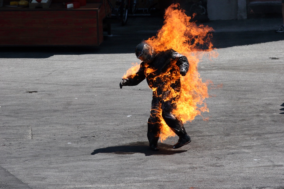 A stunt man in a jumpsuit head to toe, on fire.