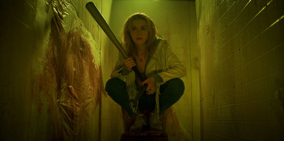 A young blonde is hiding in a dirty bathroom with a baseball bat in "Totally Killer"