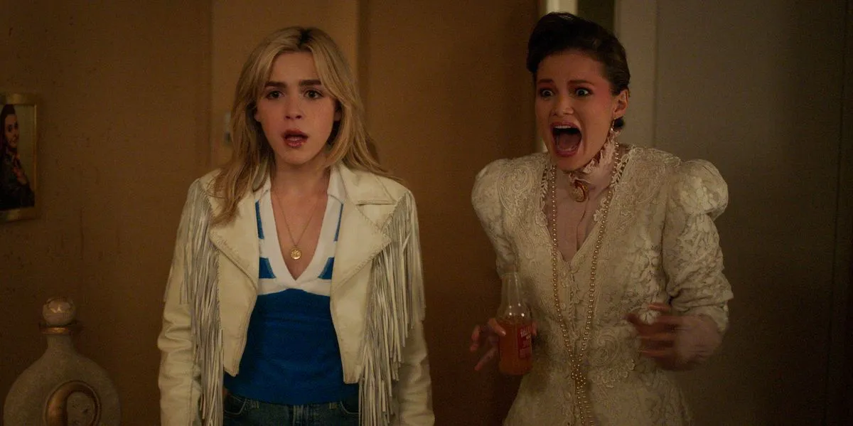 Two teen girls standing in a room, one is screaming and the other has a surprised look in the movie "Totally Killer"