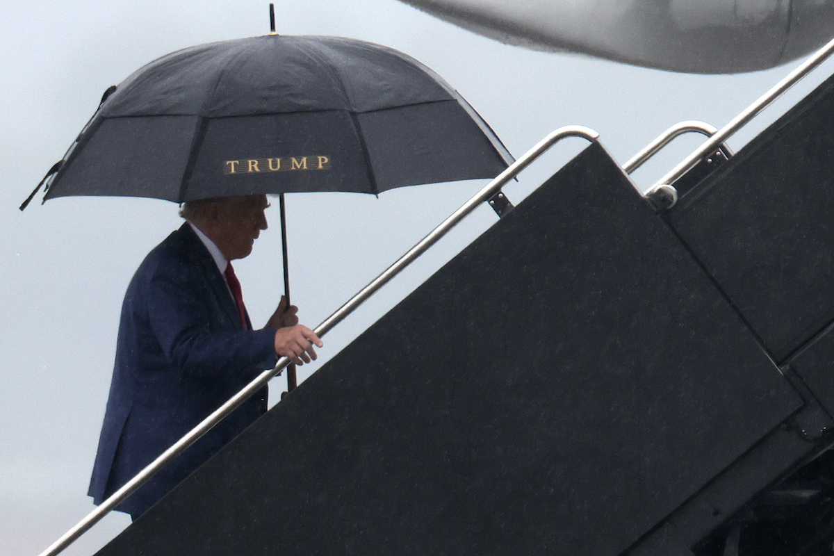 Donald Trump seen walking onto a plane, holding an umbrella bearing his name.