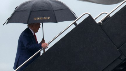 Donald Trump seen walking onto a plane, holding an umbrella bearing his name.