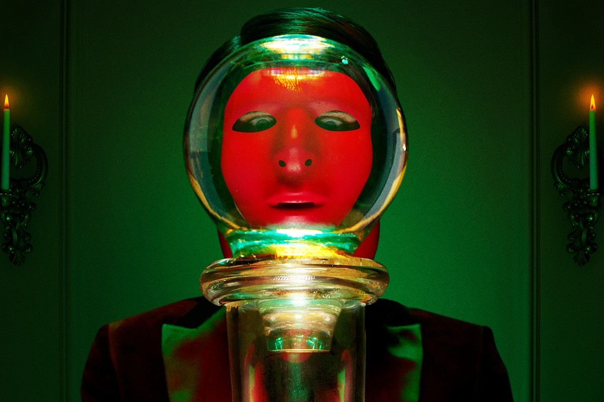 Someone wearing a red mask and looking into a class object for 'American Horror Stories' season 3