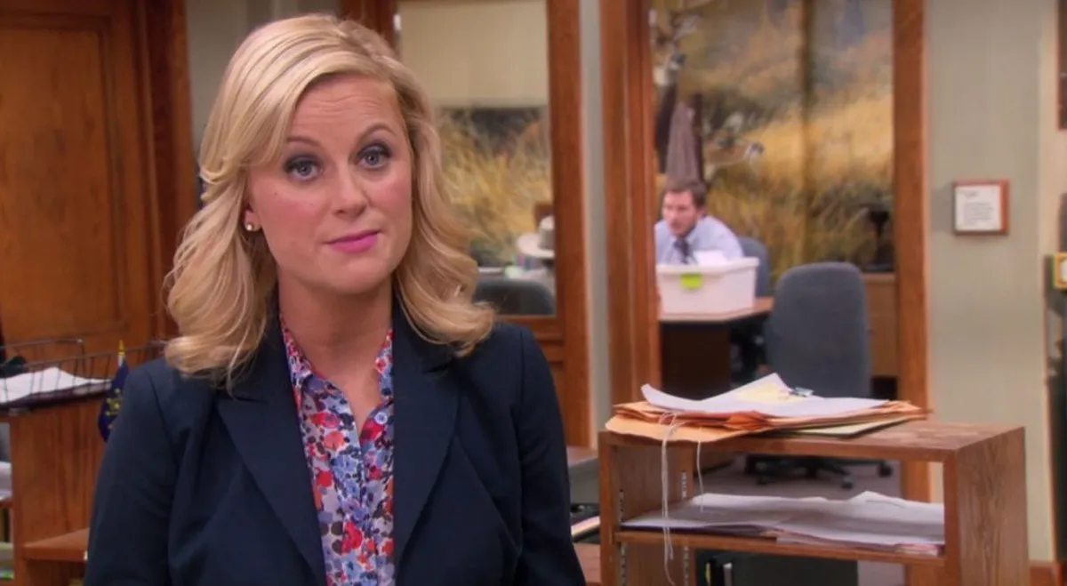 Amy Poehler as Leslie Knope looks at the camera with raised eyebrows in a government office in 'Parks and Recreation.'