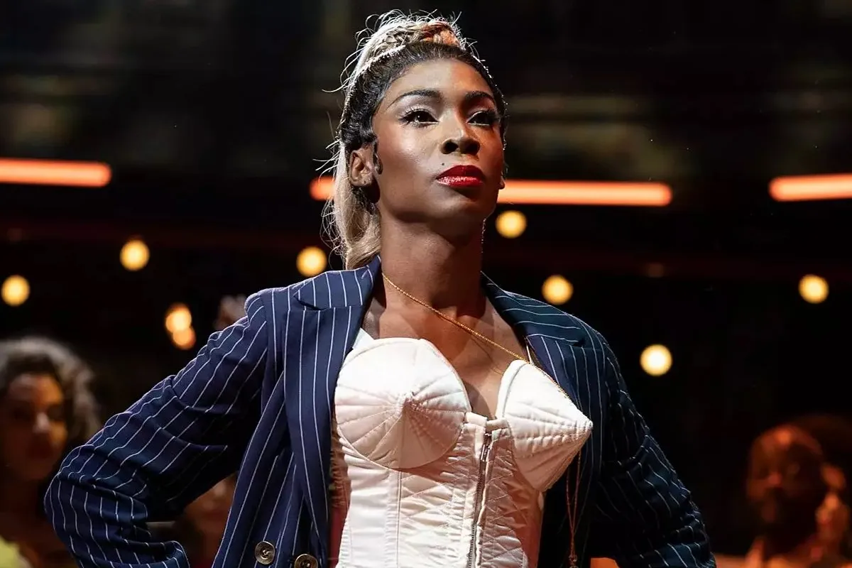 Angelica Ross in a scene from FX's 'Pose.' She is a Black trans woman styled to look like Madonna in her 'Vogue' era. She's standing in a room full of people.