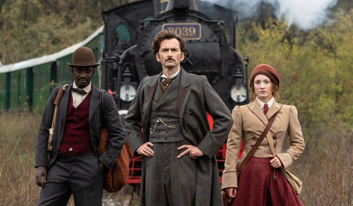 Ibrahim Koma as Passepartout, David Tennant as Phileas Fogg and Leonie Benesch as Abigail Fortescue, all standing in front of a steam train in Around the World in 80 Days