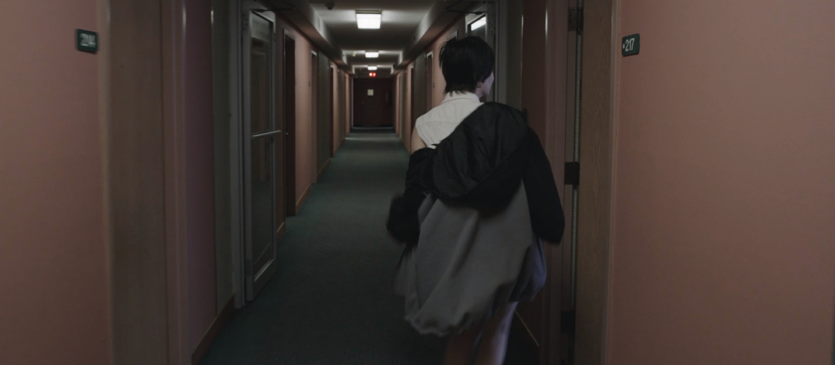 A woman walks down a hotel hallway, passing room 217 in 'Bad Things' 