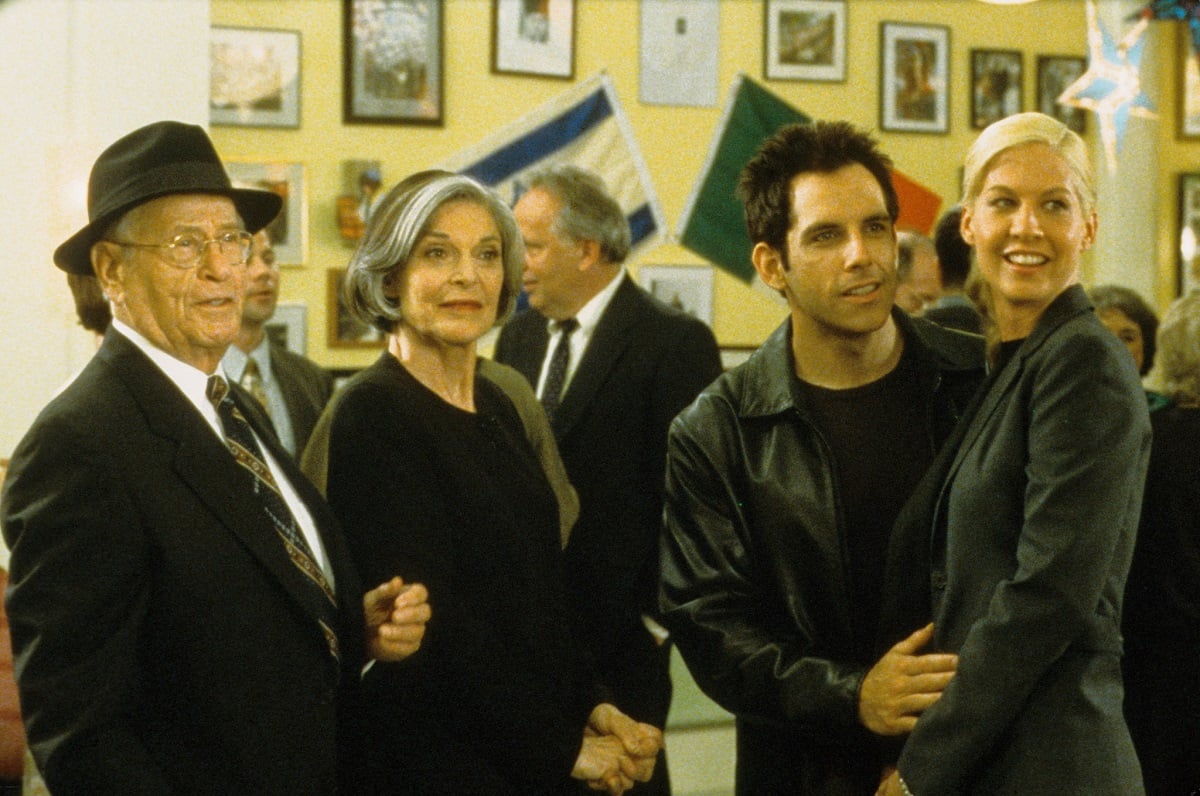 Eli Wallach, Anne Bancroft, Ben Stiller, and Jenna Elfman in a scene from 'Keeping the Faith.' Wallach is an elderly white Jewish man in a black suit wearing a black fedora. Anne Bancroft is a white woman with chin-length dark hair with a silver streak wearing a black dress. Stiller is a white Jewish man wearing a black t-shirt under a black leather jacket. Elfman is a white Jewish woman with blonde hair wearing a black suit. They stand together at a party.