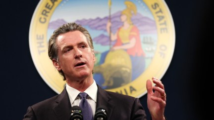 California Governor Gavin Newsom stands in front of the CA seal.