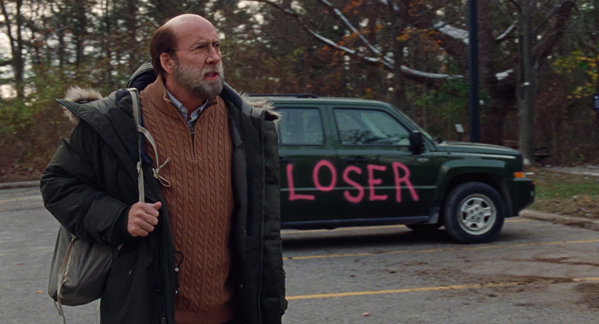 Nicolas Cage stands in front of a car spraypainted with the word "Loser" in this photo still from 'Dream Scenario'.