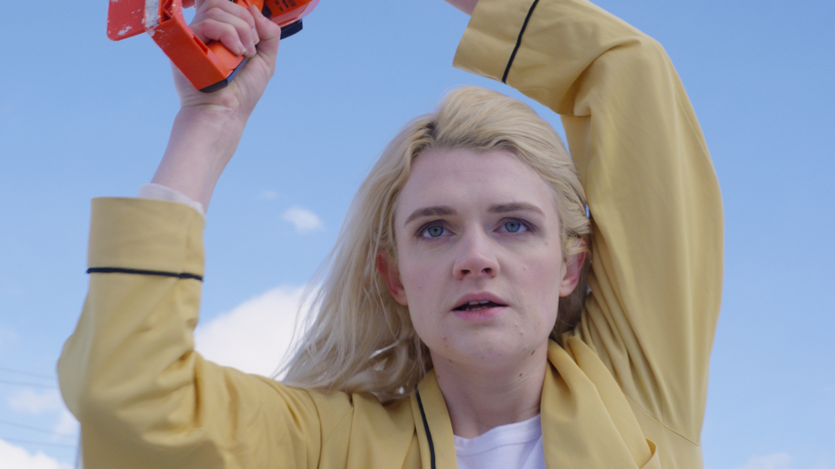 Gayle Rankin wielding a chainsaw under a blue sky in the horror movie 'Bad Things'