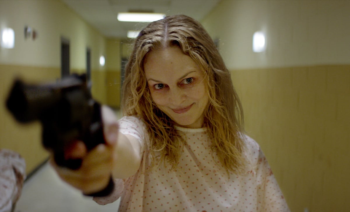 Heather Graham wears a hospital gown while holding a gun and smiling in the new horror movie 'Suitable Flesh'