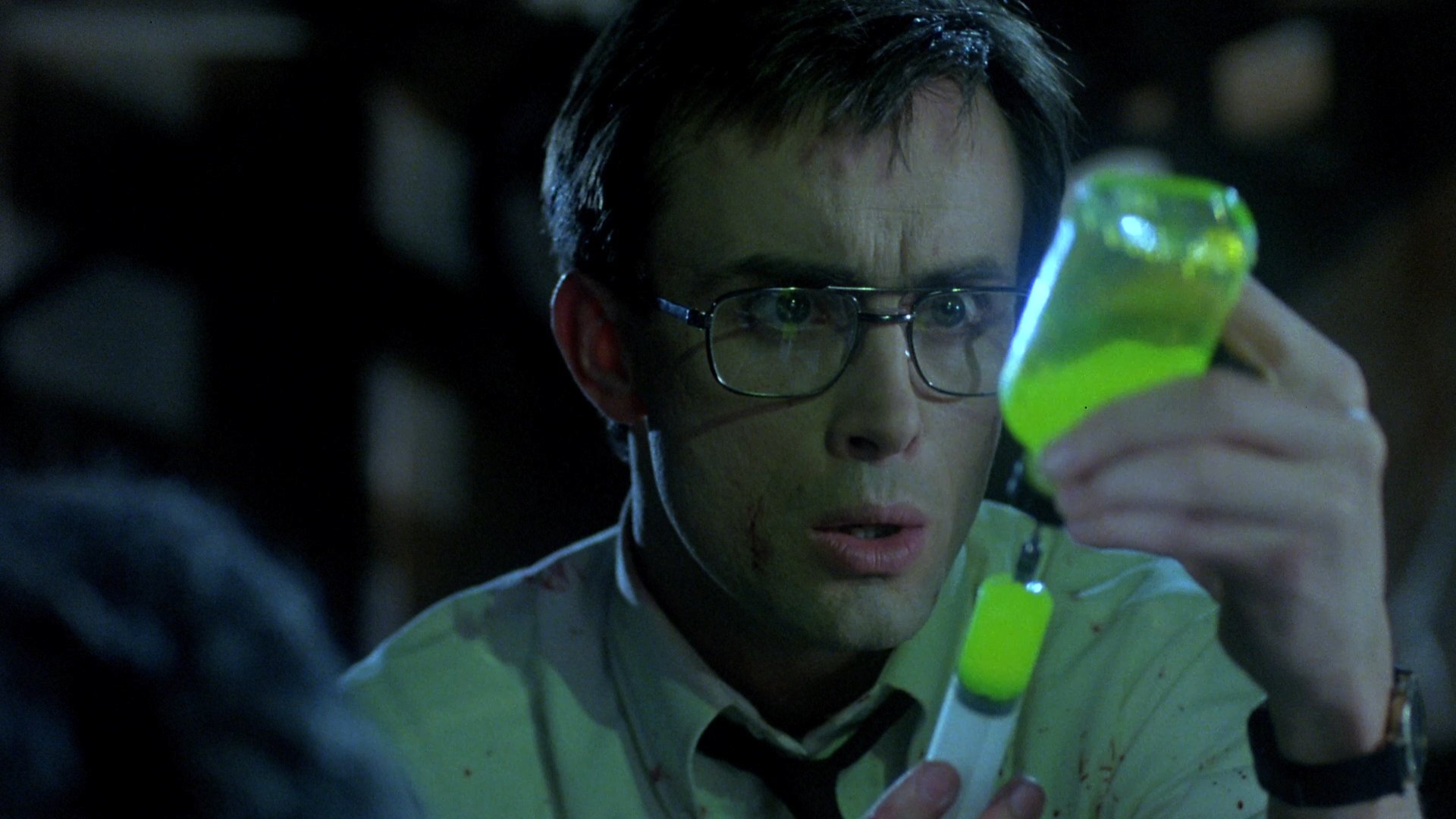 A bespectacled Herbert West (Jeffrey Combs) extracts a bright green “re-animating agent” from a vial in ‘Re-Animator.’ 