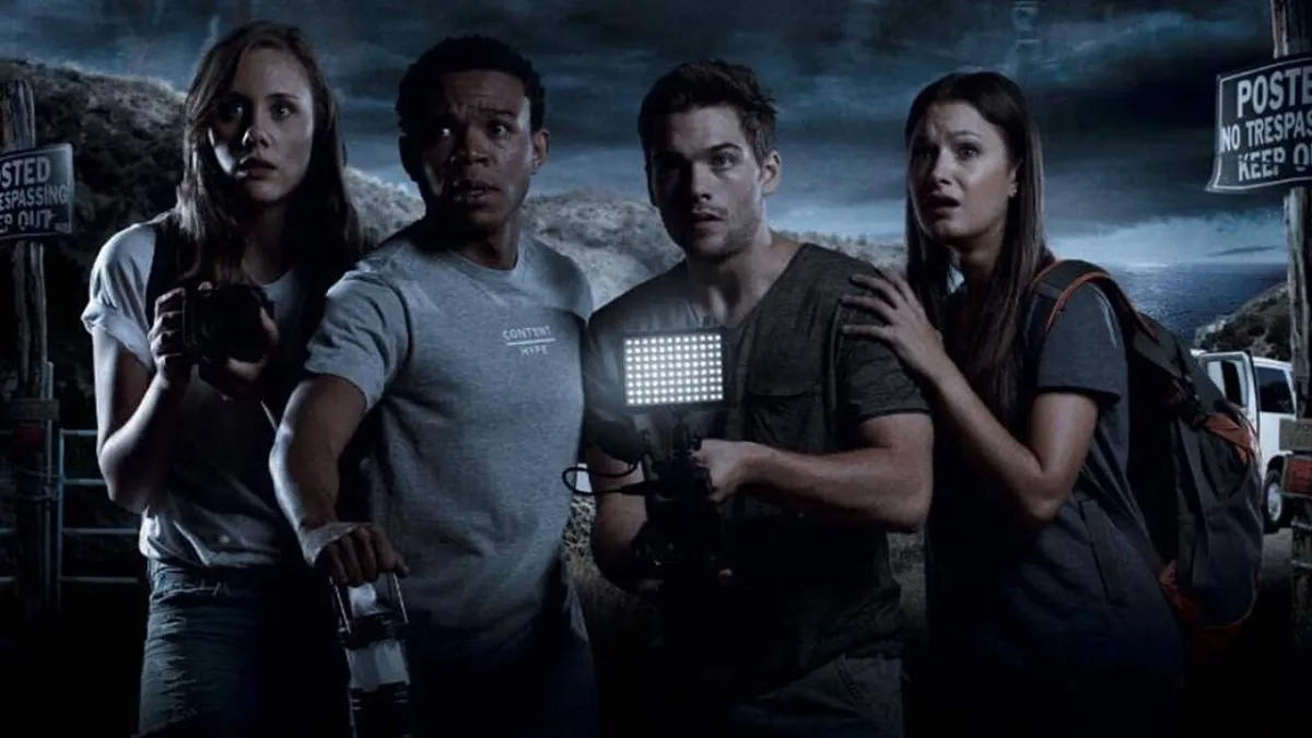 Rebecca Forsythe, Robert Bailey Jr., Dylan Sprayberry, and Valentina de Angelis in a scene from 'Malibu Horror Story.' They are standing in a row looking at something ahead of them that's scary holding cameras and lanterns. 