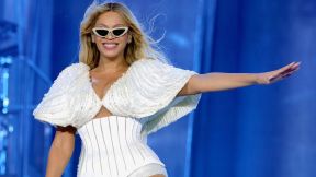 Beyonce performs and grins in a white outfit and sunglasses.
