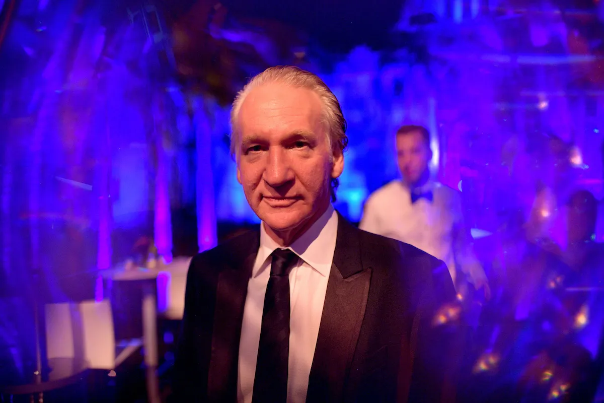 Bill Maher at a party with a purple lighting effect around him.
