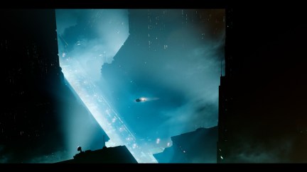 Still image from Blade Runner 2033: Blade Runner 2049; a nightime cityscape in shades of electric blue and black, with massive towers and a tiny ship moving between them.