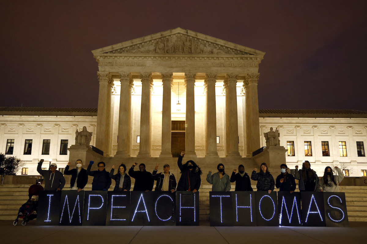 Protesters hold a large banner in front of the Supreme Court building at night, reading "Impeach Thomas"