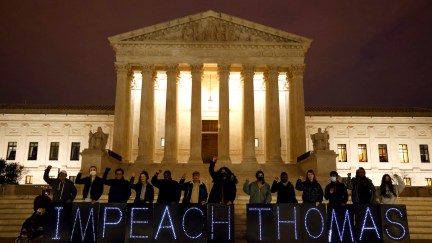 Protesters hold a large banner in front of the Supreme Court building at night, reading 