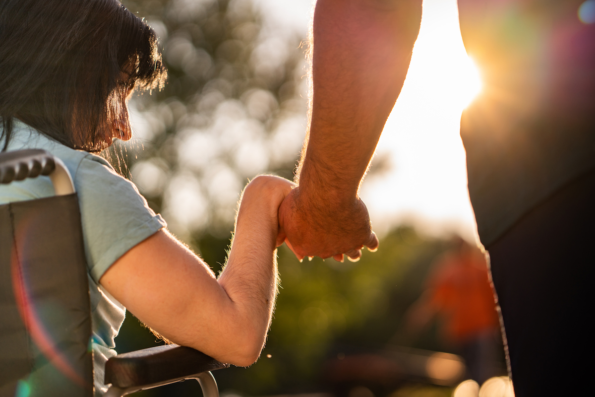 Close up on a woman in a wheelchair holding a man's hand at sunset