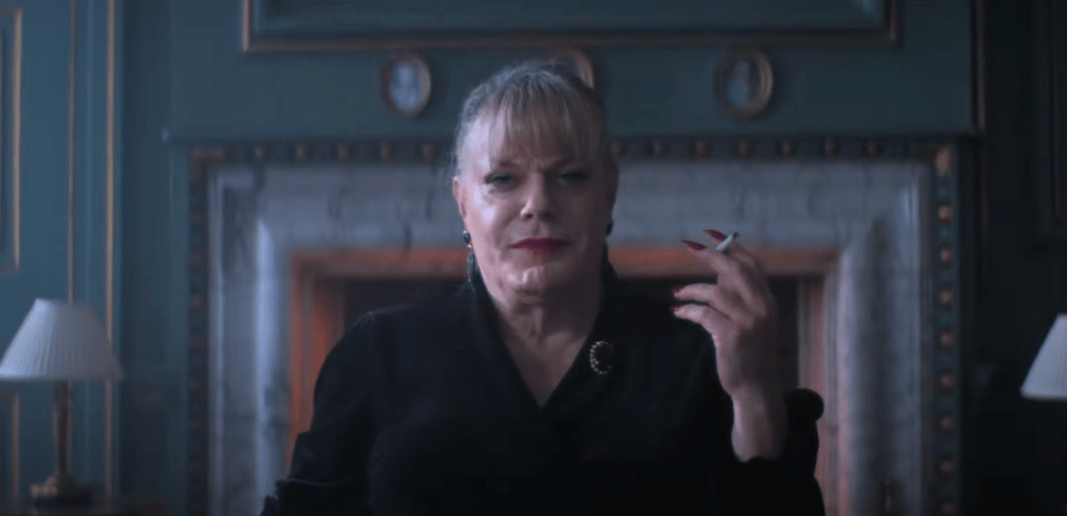 Dr. Jekyll (Eddie Izzard) smiles into the camera, holding a cigarette and sitting in a gothic-looking room.