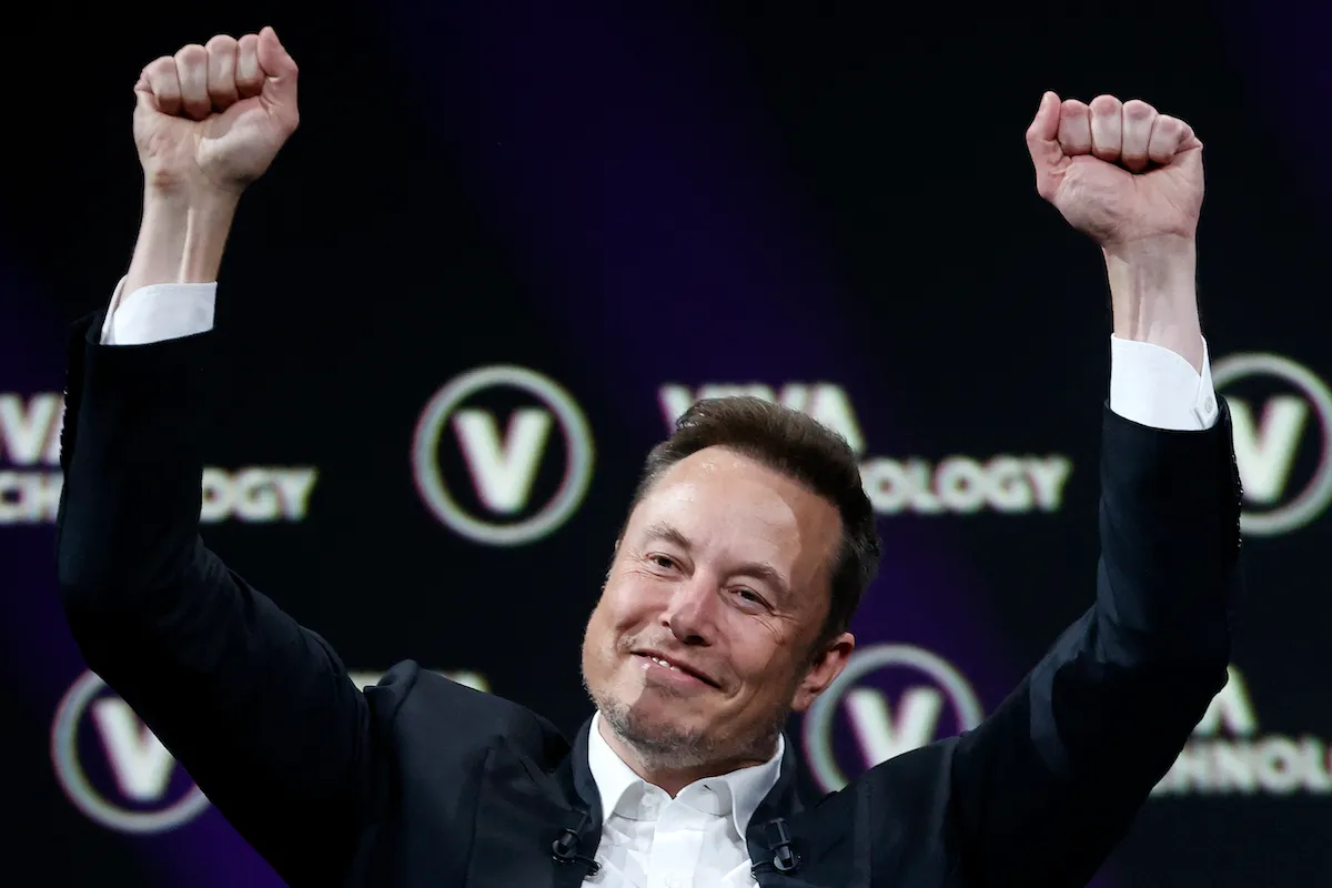 Elon Musk holds his fists above his head in mock triumph.
