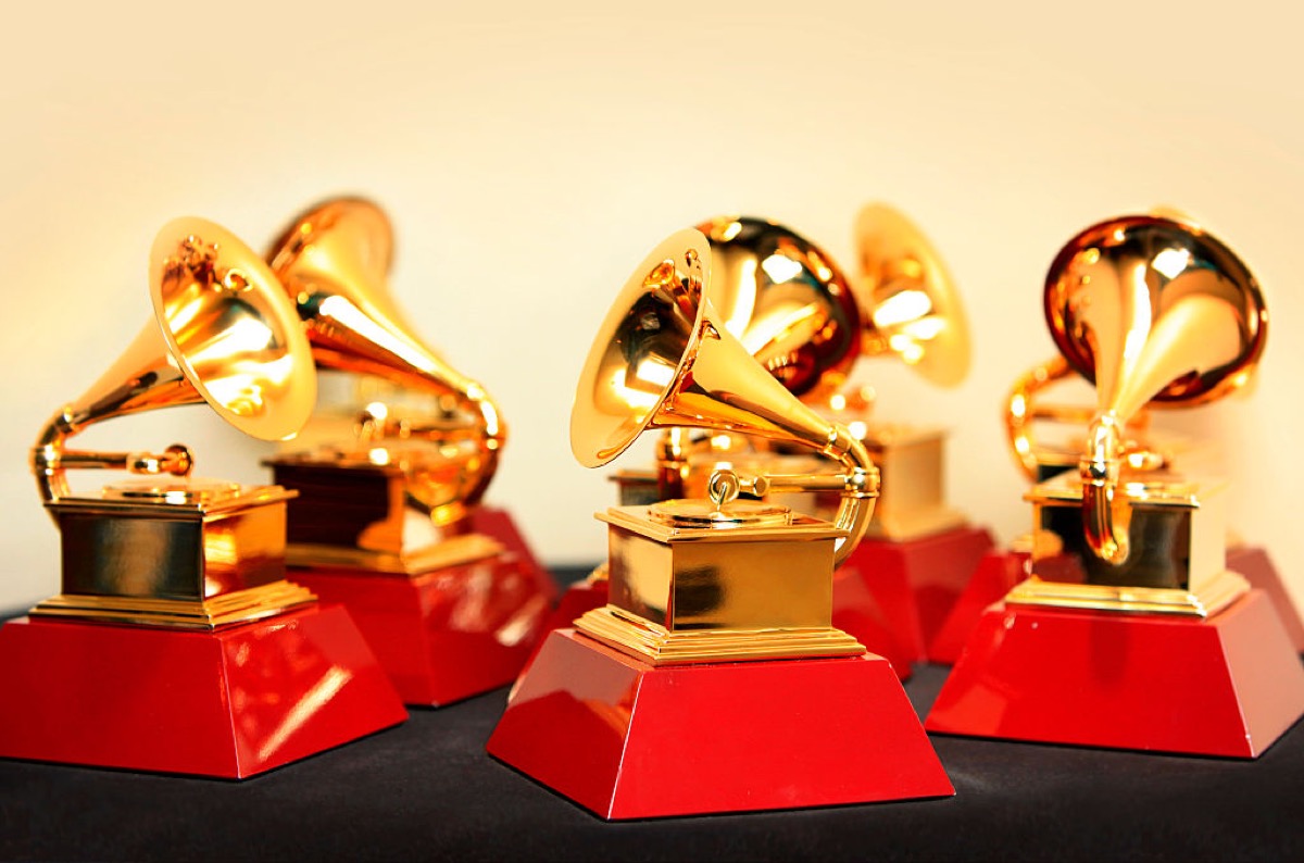 A group of Grammy award statues sitting together on a table against a blank golden background.