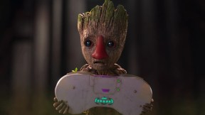 Baby Groot wears a fake human nose while holding a controller as big as his body.