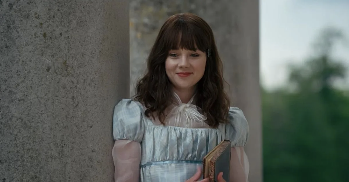 A white woman in a pale blue regency dress smiles while holding a book in "Bridgerton"