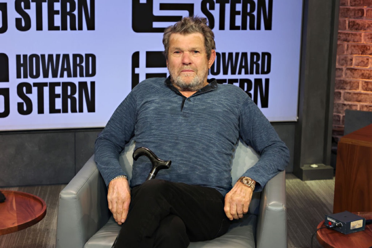 Jann Wenner on the Howard Stern Show. He reclines in a chair, looking somewhat uncomfortable.