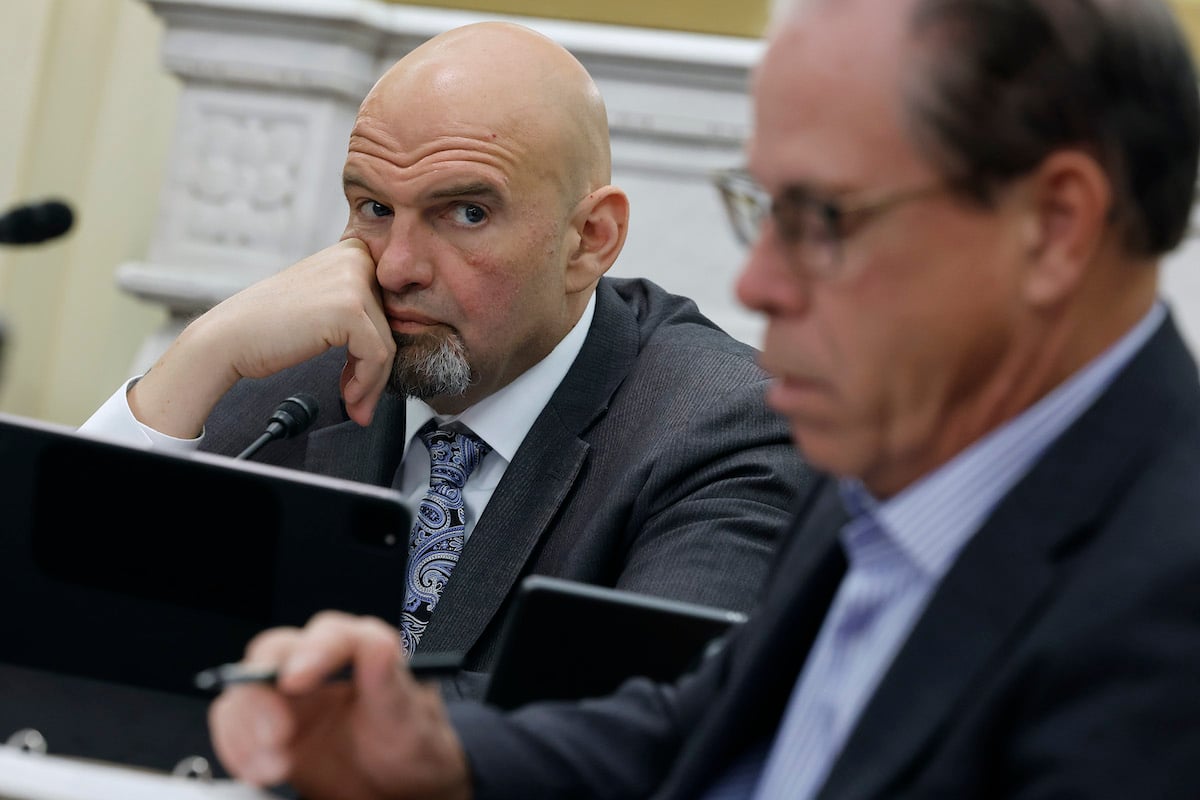 John Fetterman wears a suit, rests his chin on his hand looking annoyed.