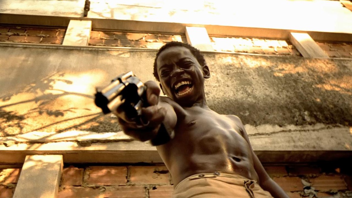 A young boy holds a pistol and gleefully prepares to shoot someone beneath him in "City of God"