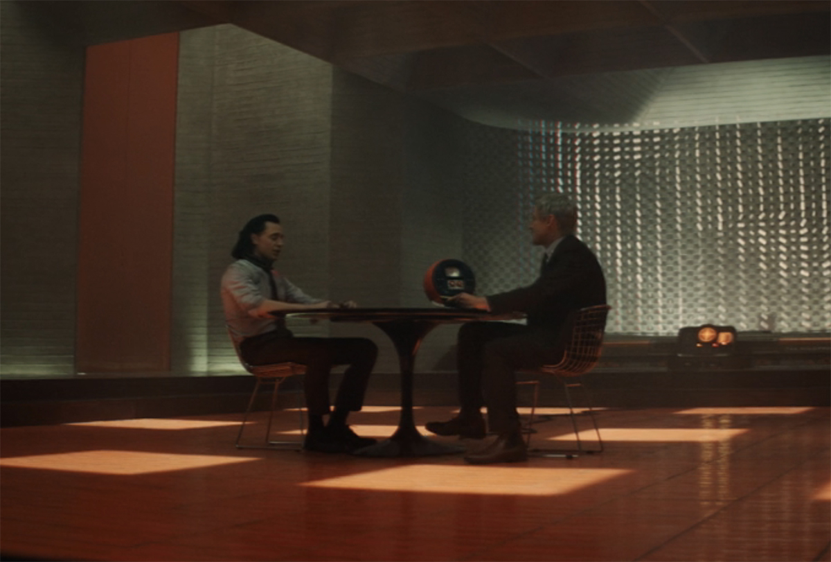 Mobius talking to Loki at a table in the TVA