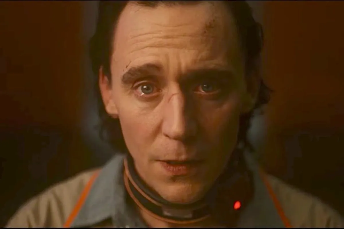 Loki stares into the camera with tears welling up in his eyes. He's wearing his TVA prisoner's uniform.