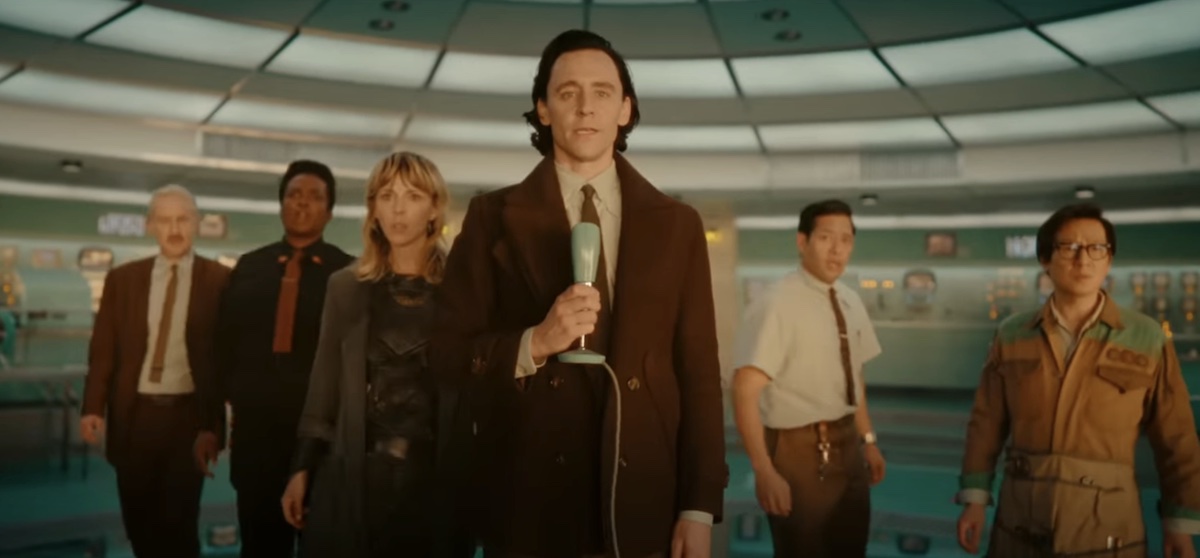Loki holds a microphone, with Mobius, B-15, Sylvie, Casey, and O.B. standing behind him.