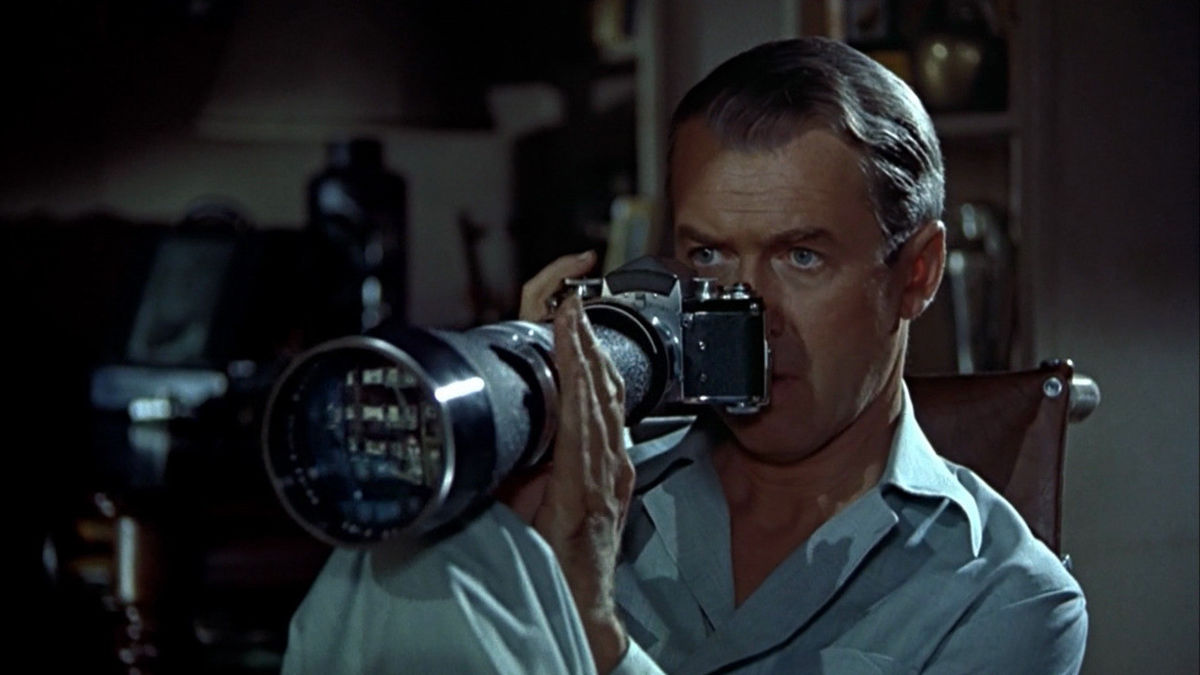 Jimmy Stewart peering out the window with a camera in "Rear Window"