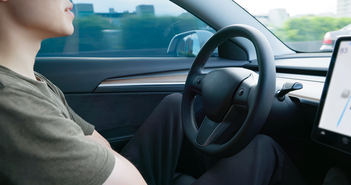 A driver sits with their arms crossed behind the wheel of a car.