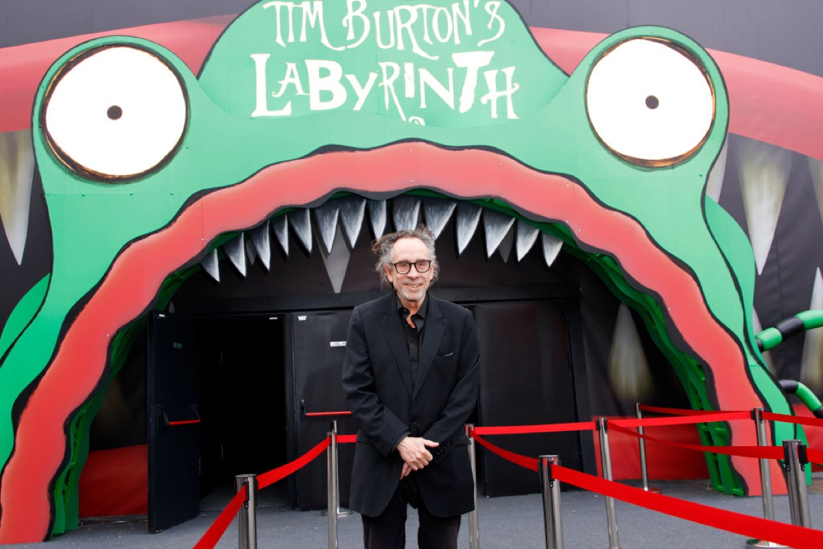 Tim Burton stands in front of a huge placard of a monster's mouth, which covers a door.