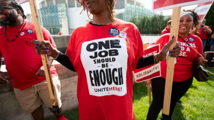 Striking workers holding picket signs. One Black woman wears a shirt reading 