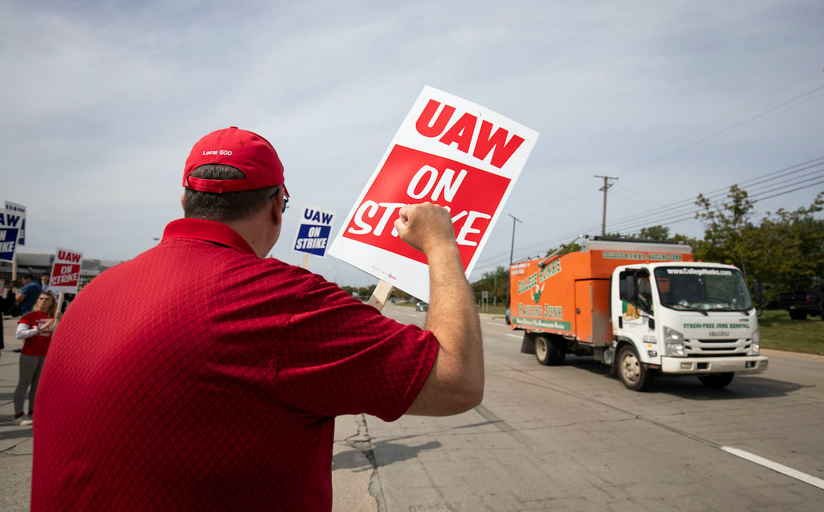 A man holding a UAW on Strike sign raises his fist to passing cars.