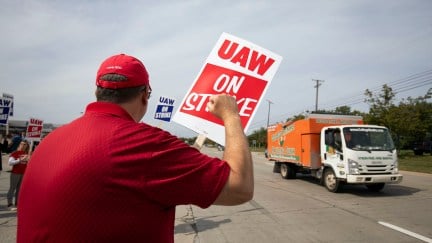 A man holding a UAW on Strike sign raises his fist to passing cars.