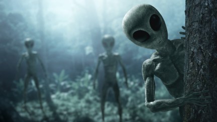 Alien creatures peek out from behind trees in the forest